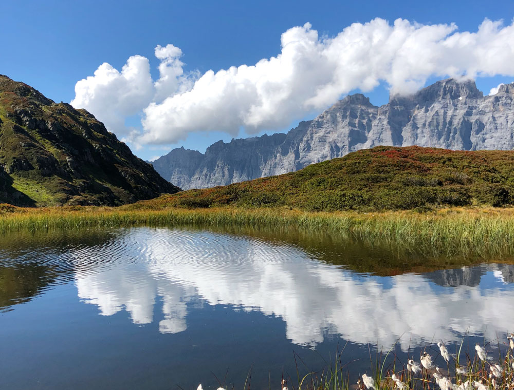 Swiss countryside with mountains and lake reflecting fluffy white clouds in a blue sky