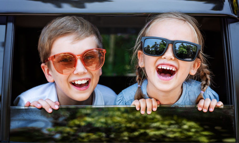 Young boy and girl wearing sunglasses laughing through an open car window