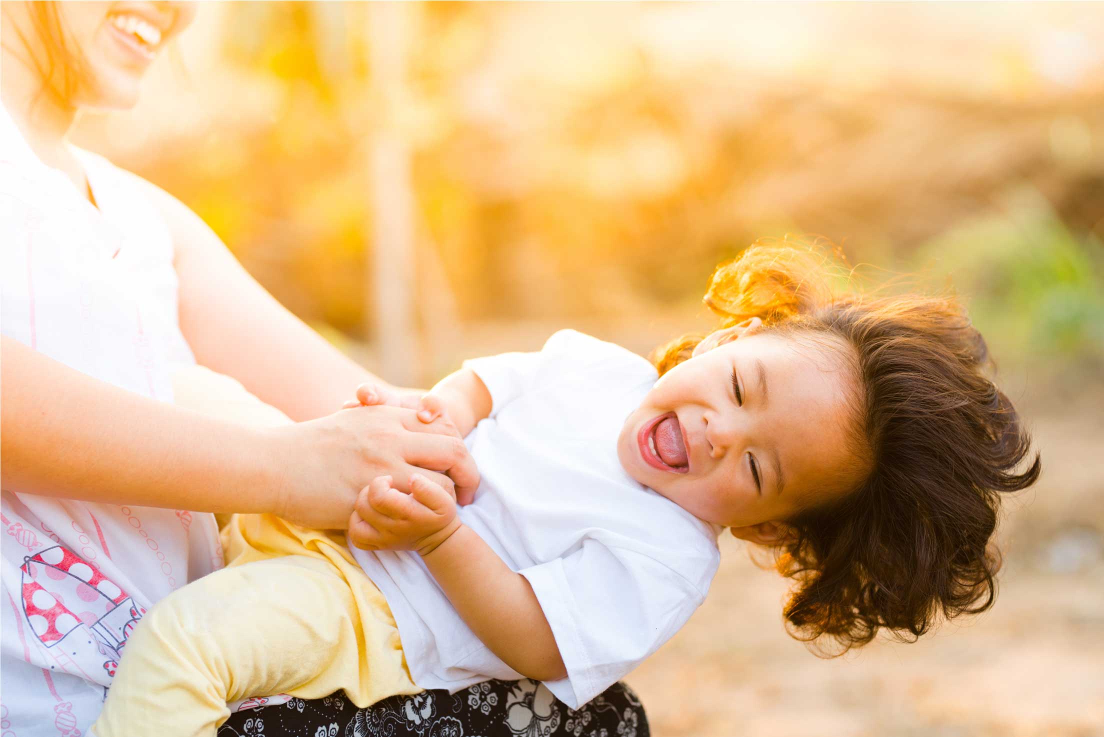 Woman swinging laughing young boy around in the setting sun