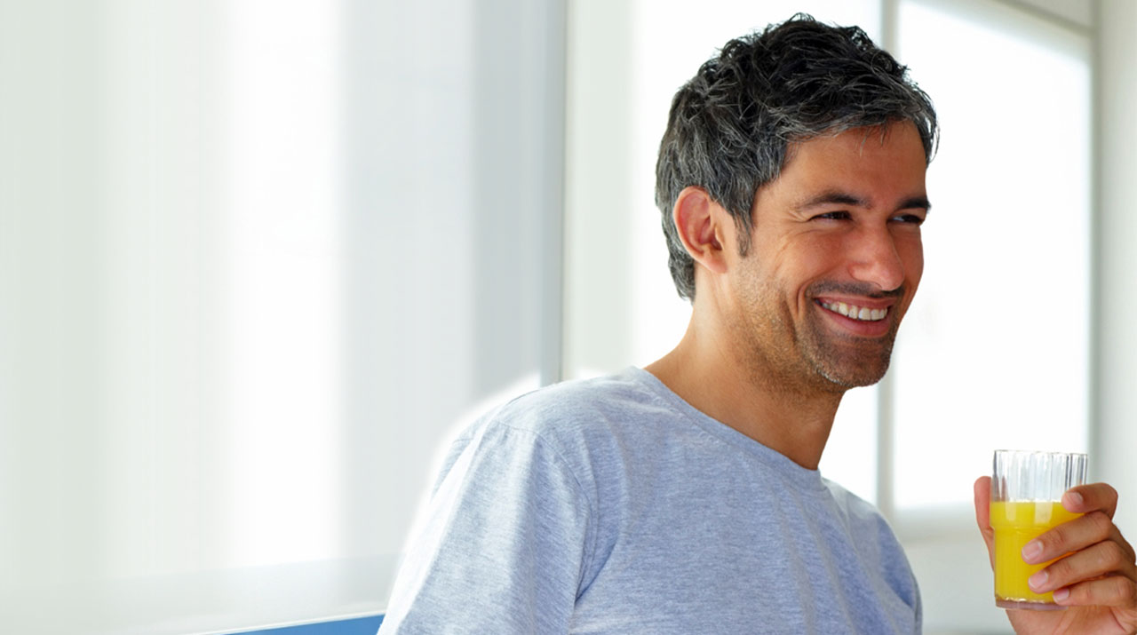 Man smiling while holding a glass of orange juice